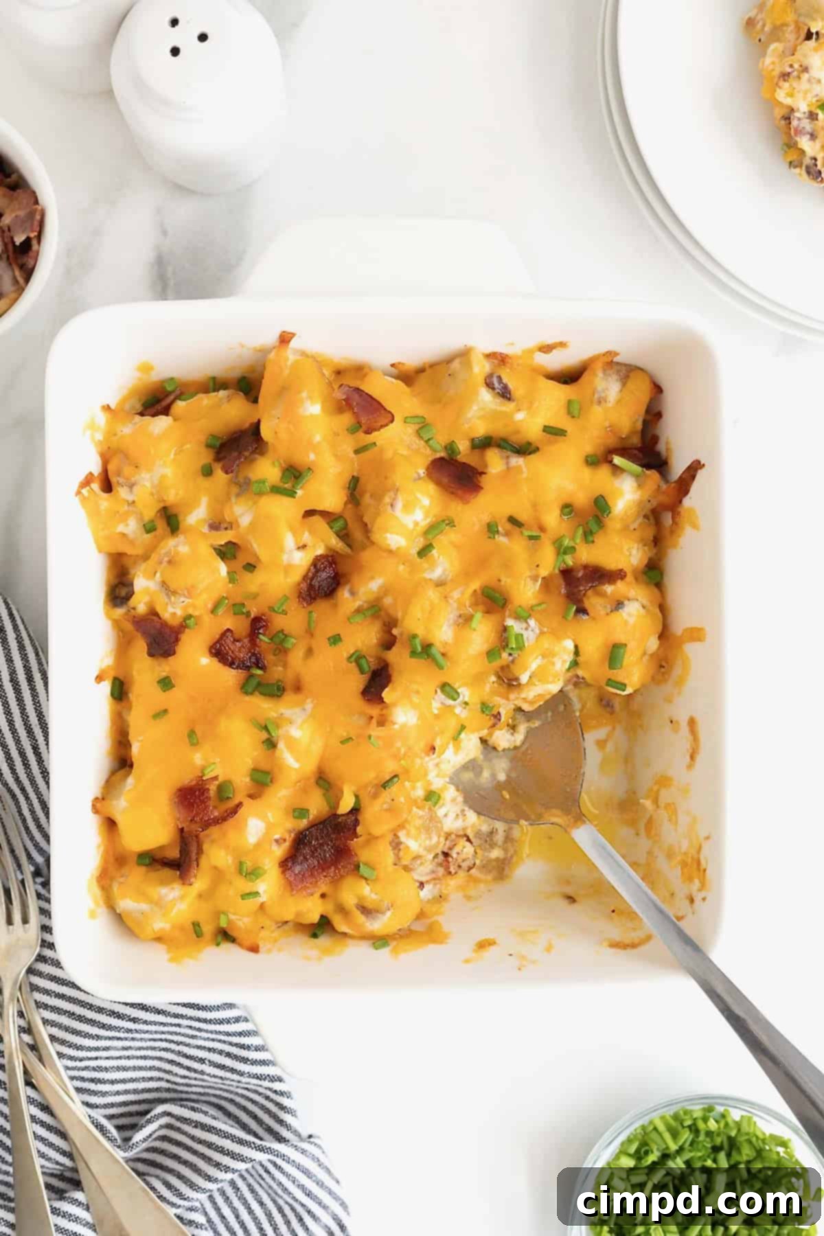 A square white baking dish of potato casserole topped with bacon bits and melted cheese.