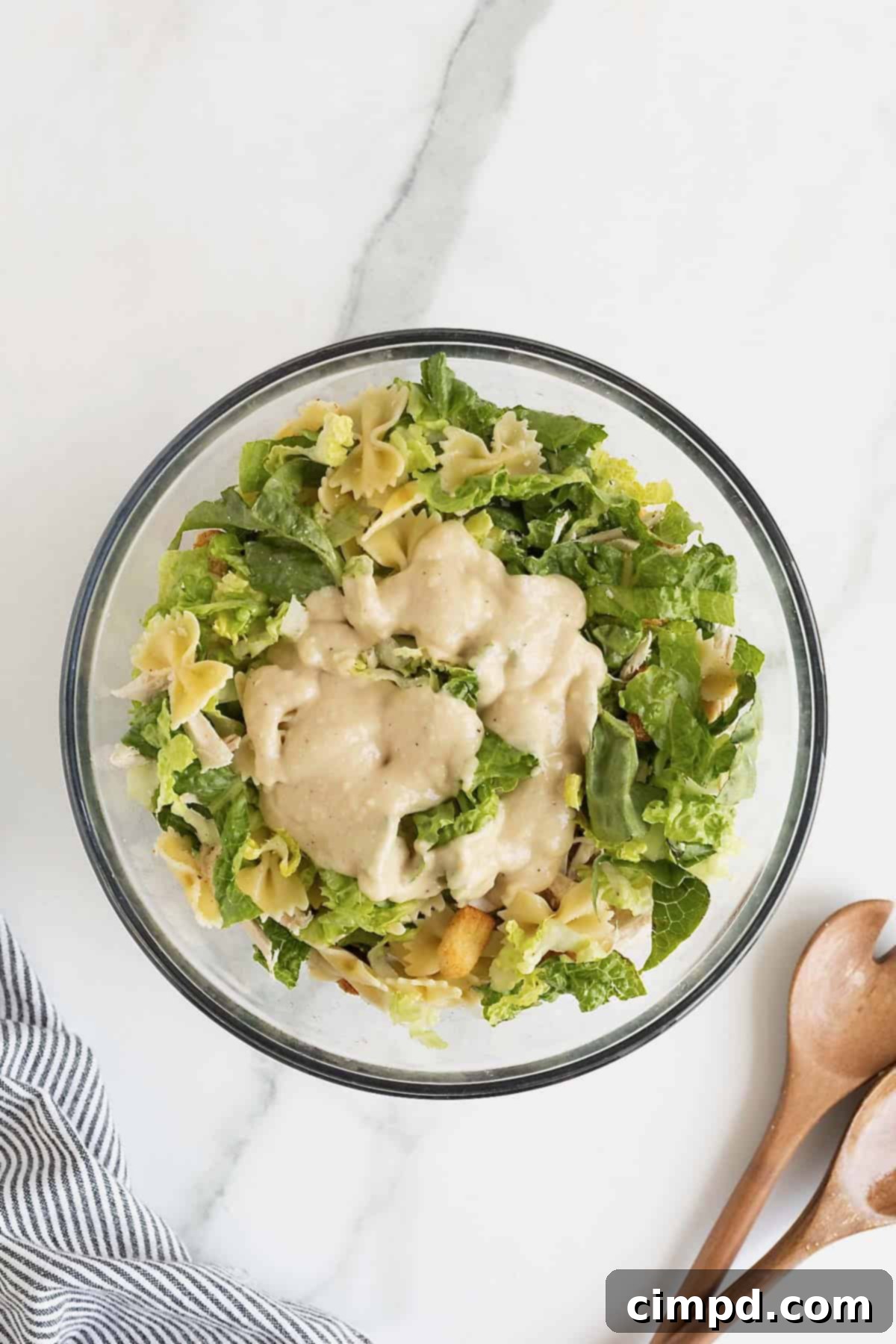 Caesar dressing on a salad in a large glass mixing bowl.