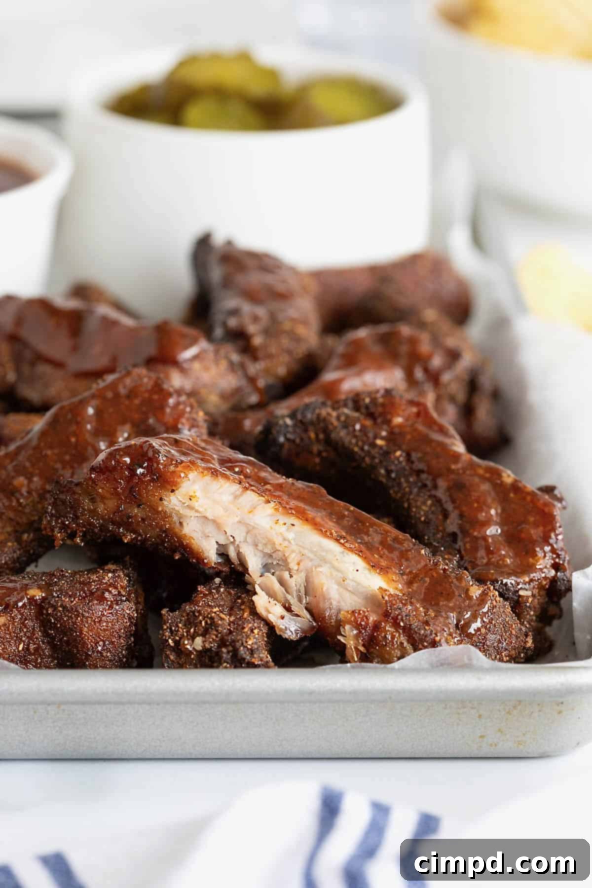 A close-up shot of a baby back rib with a bite taken out, resting on a parchment-lined rimmed aluminum baking sheet, highlighting its tender, juicy meat.
