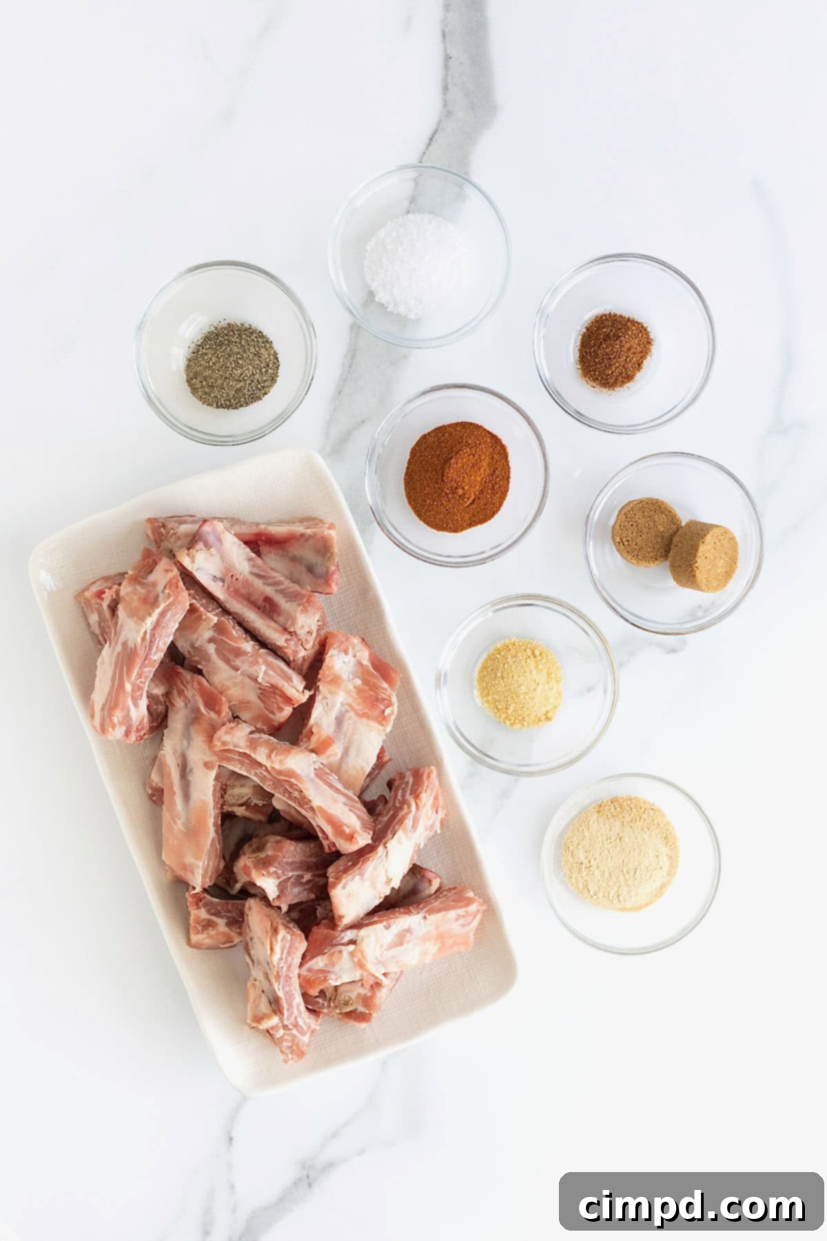 A collection of small glass dishes containing all the dry rub ingredients laid out on a white marble counter, ready for mixing.