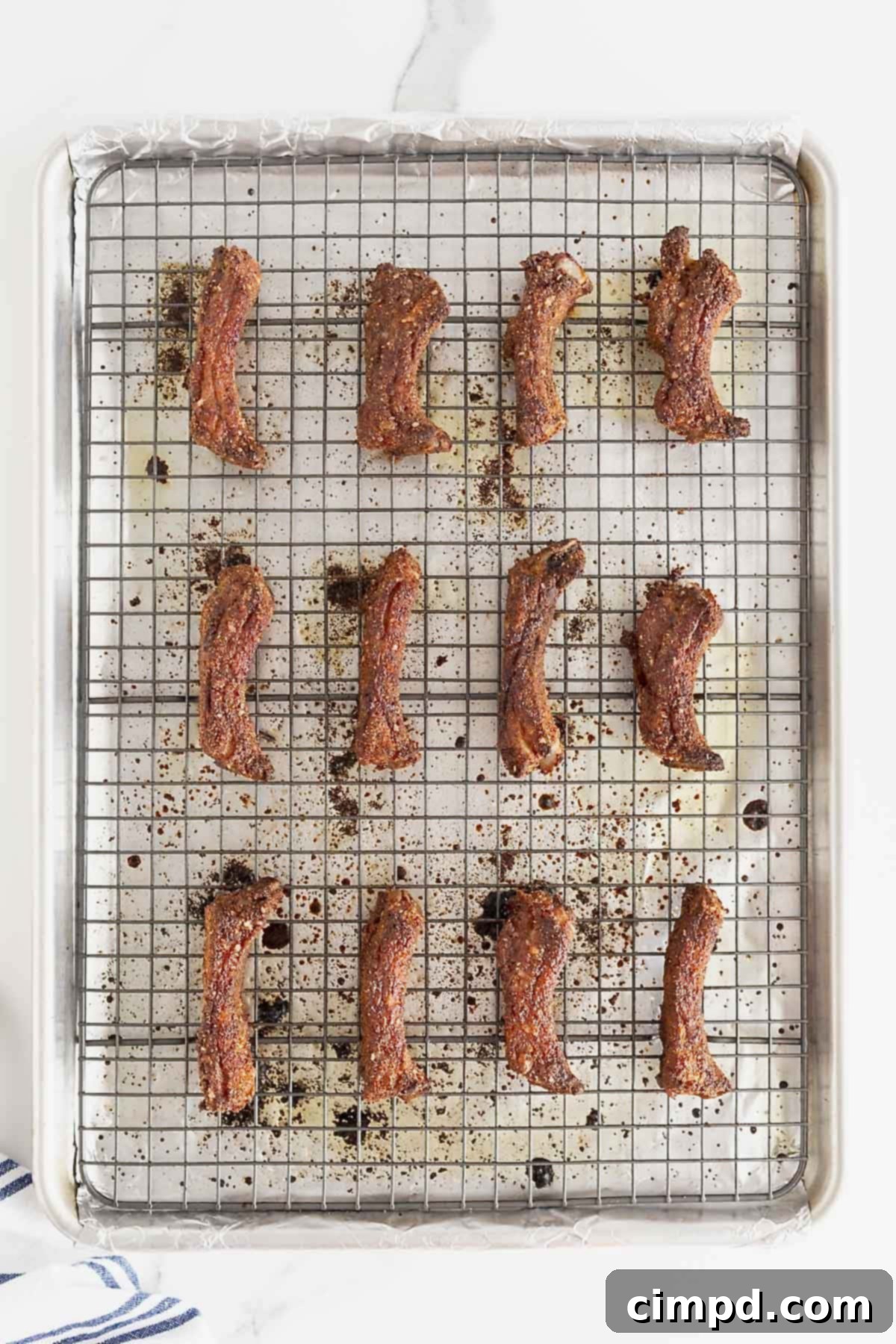 Twelve perfectly baked baby back ribs arranged on a wire rack positioned over a prepared baking sheet, showcasing their golden-brown color and crispy crust.