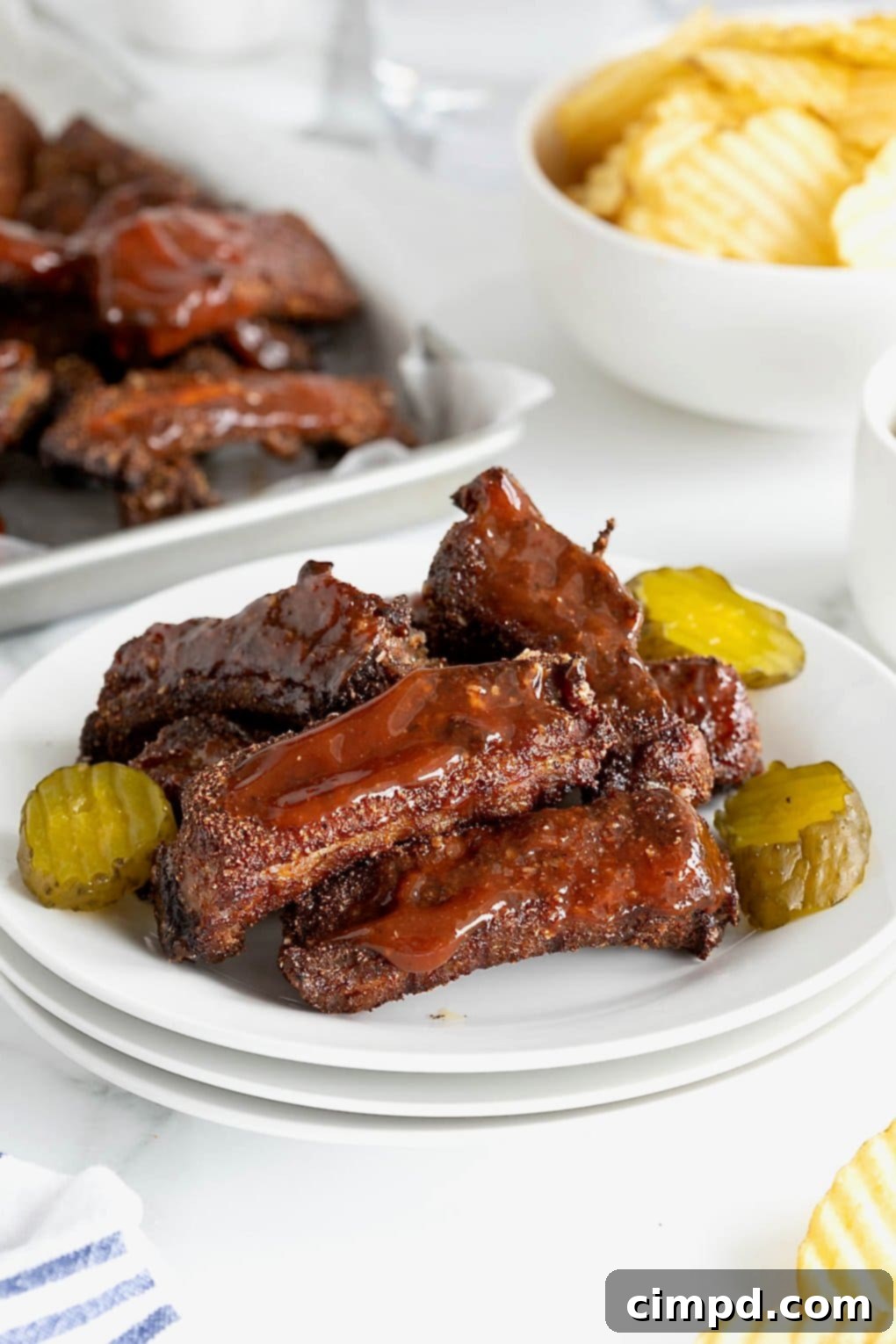 A beautifully arranged plate of individual baby back ribs, garnished with pickle slices and a generous dollop of barbecue sauce, ready to be devoured.