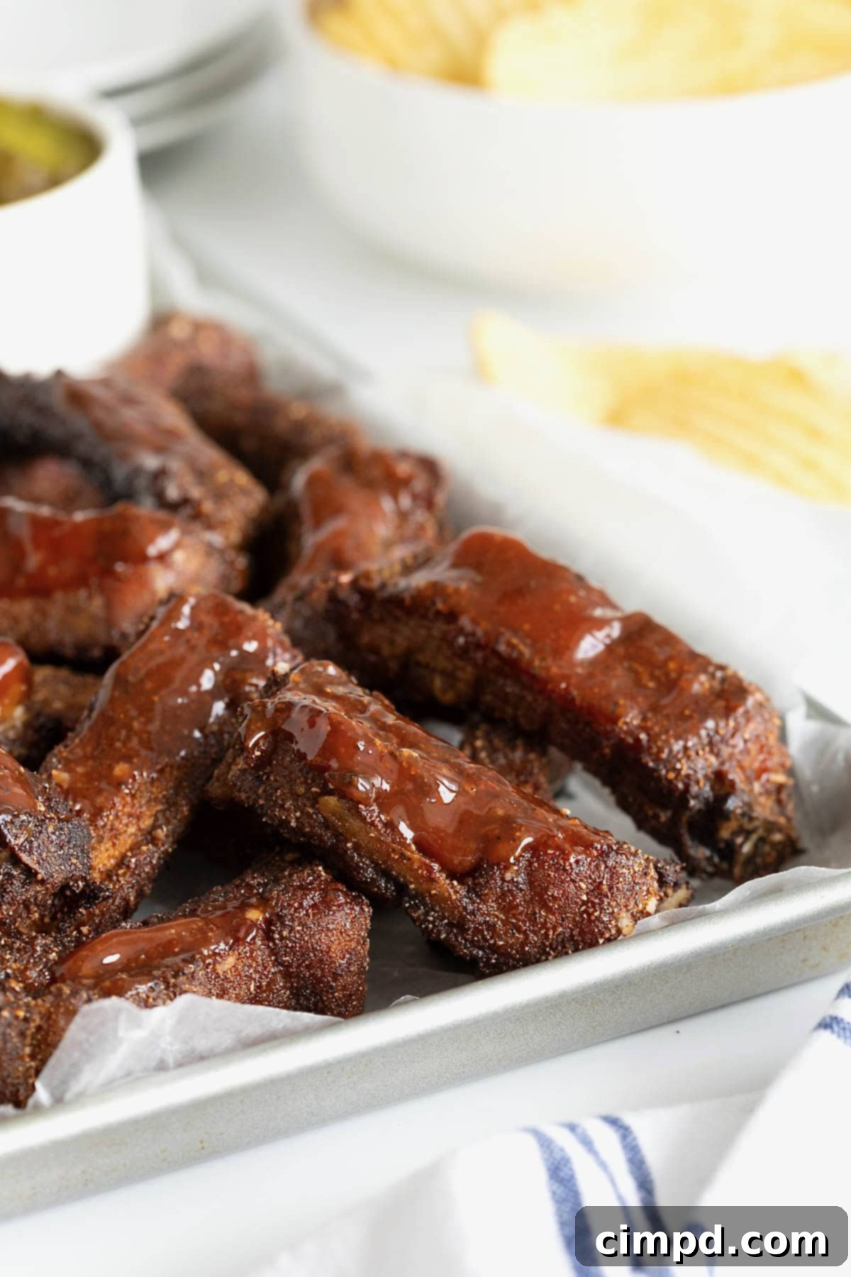 A generous pile of dry-rubbed baby back ribs, drizzled with barbecue sauce, resting on a parchment-lined aluminum rimmed baking sheet.