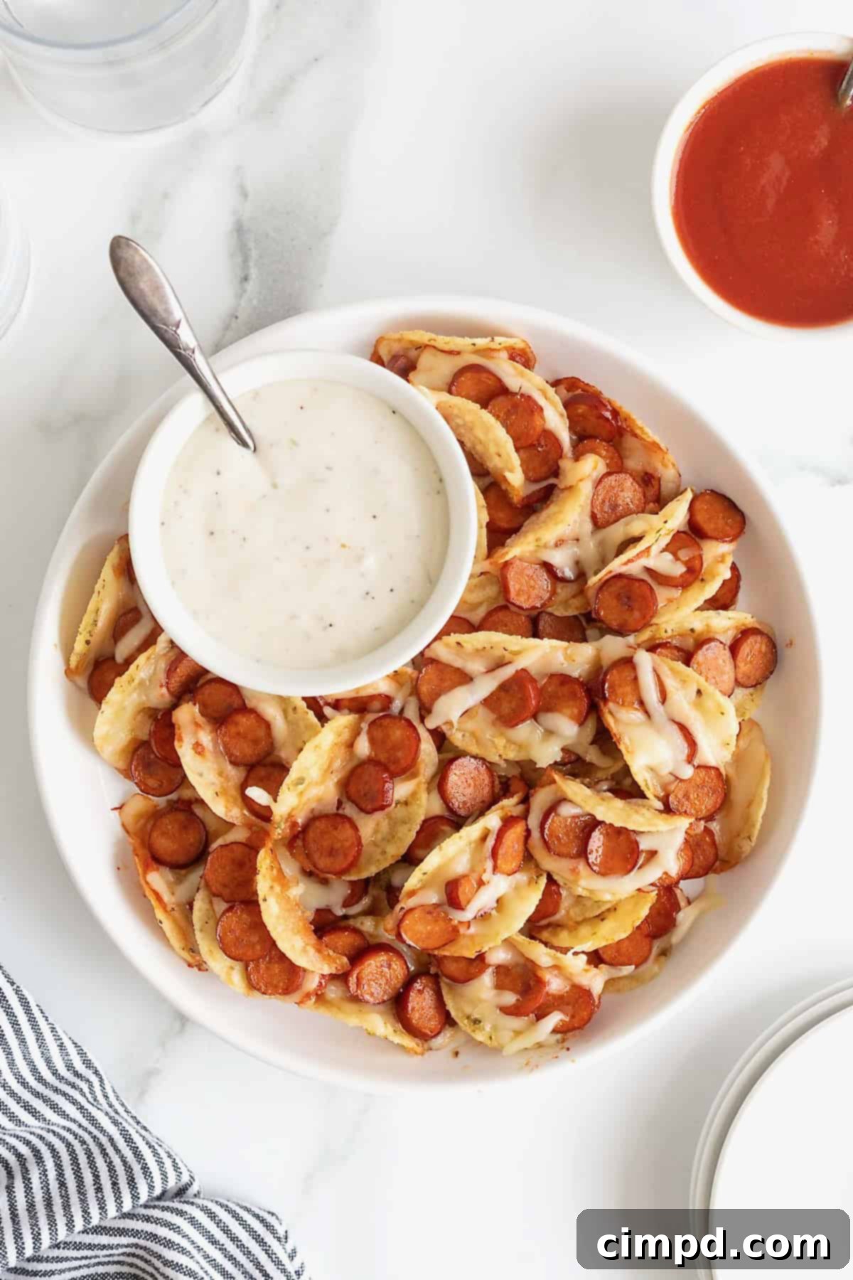 A large rimmed white serving plate piled with pizza taco bites. There is a small white dish of ranch dipping sauce.