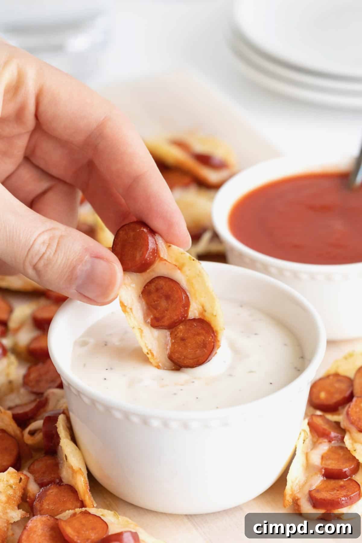 A pizza taco bite being dipped in ranch dressing in a small white dish.