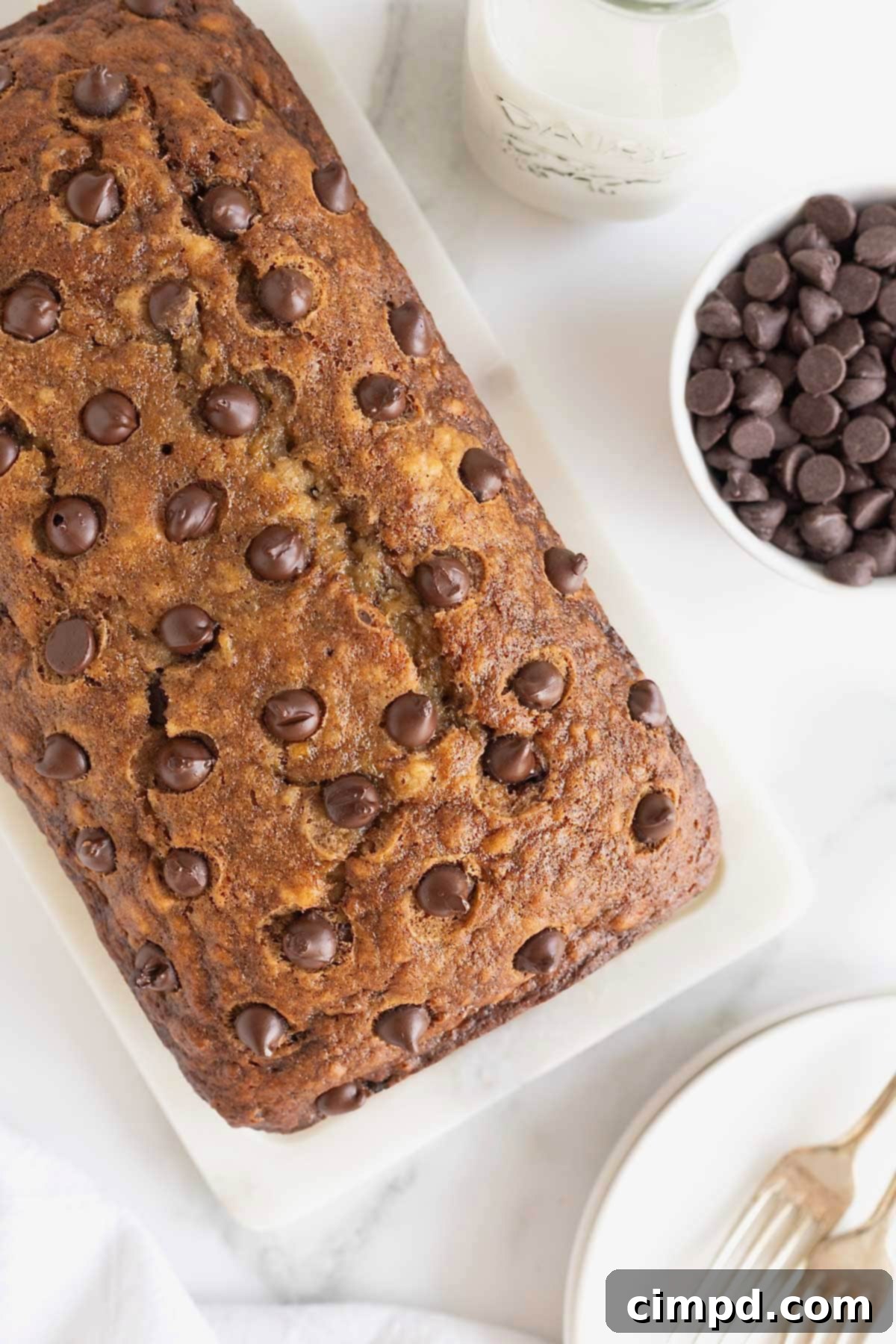A loaf of brown butter banana bread studded with chocolate chips on a white surface.