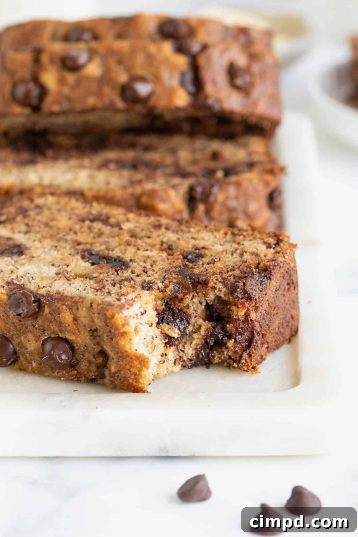 A slice of brown butter banana bread with chocolate chips on a white cutting board. There is a bite taken out of the bread.