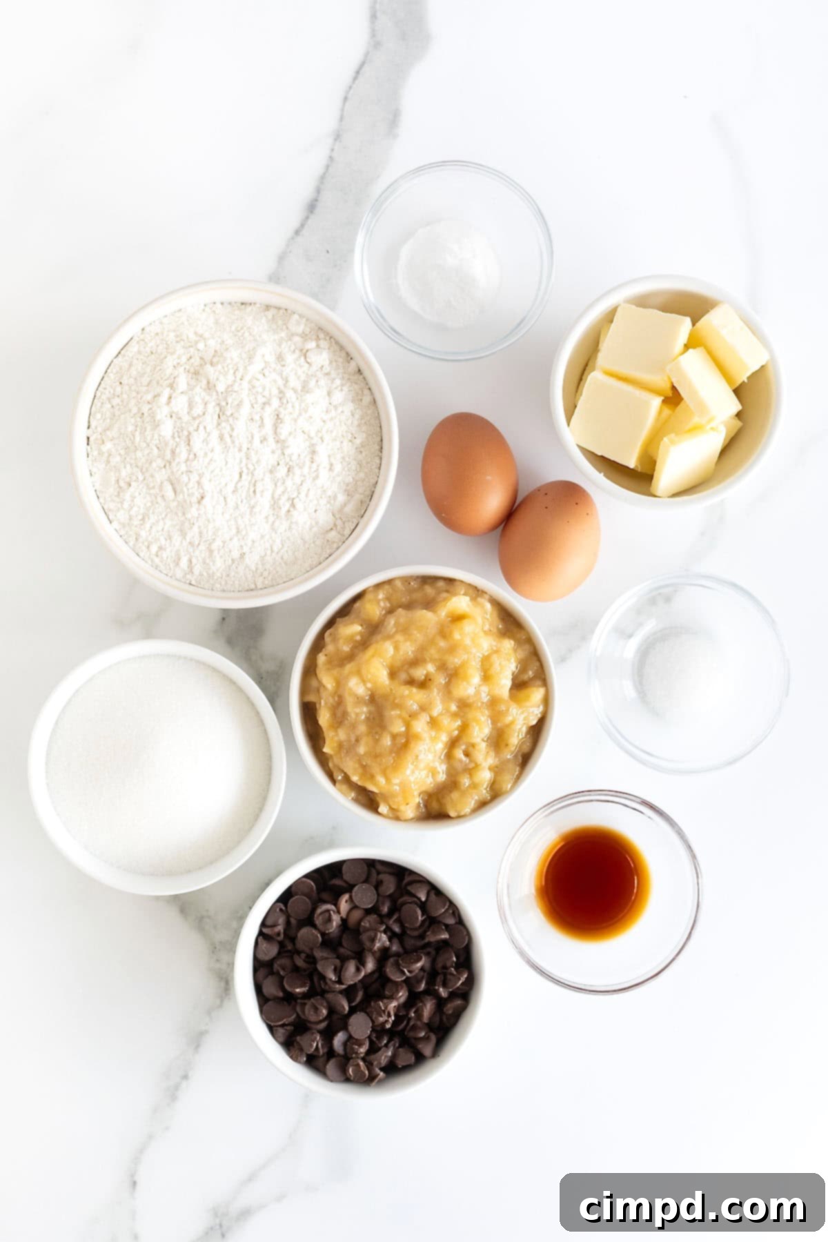 Ingredients to make brown butter banana bread with chocolate chips in small white dishes on a white marble counter.