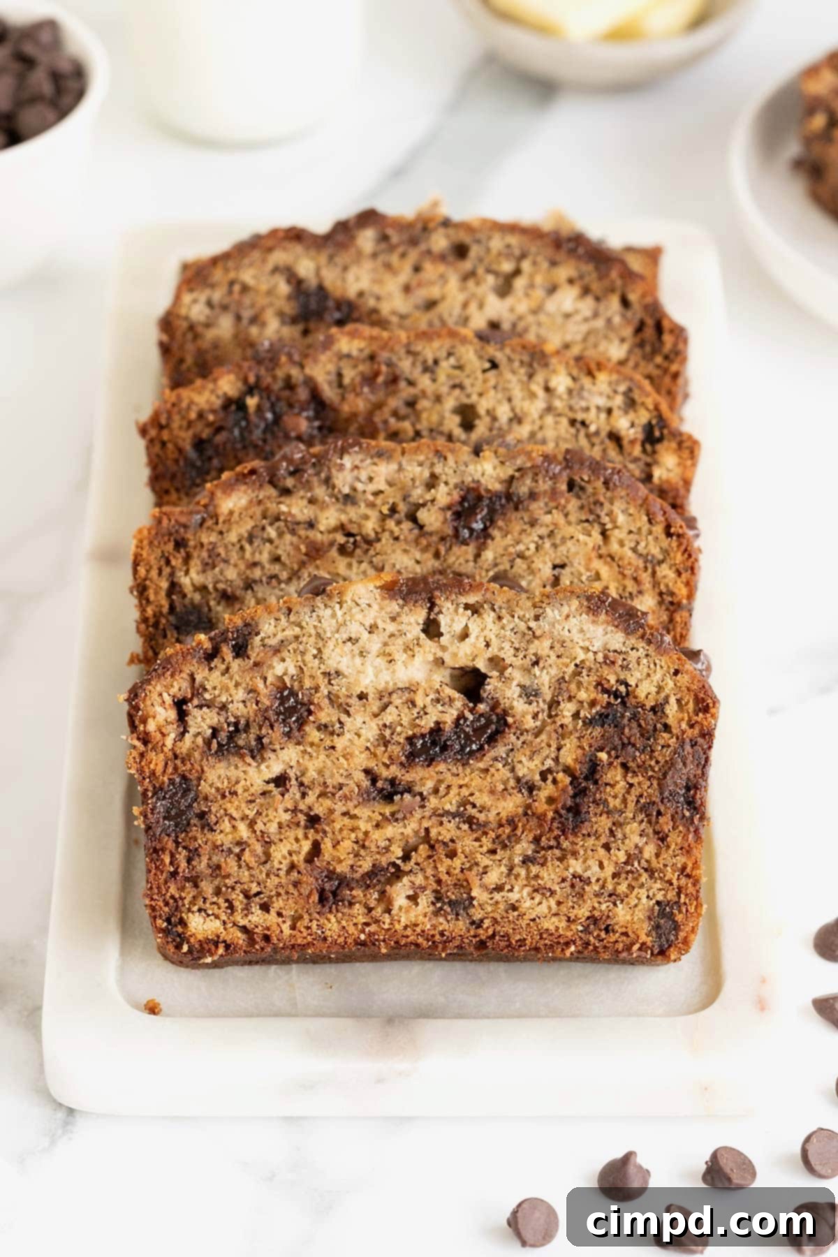 Four slices of chocolate chip brown butter banana bread on a white cutting board.
