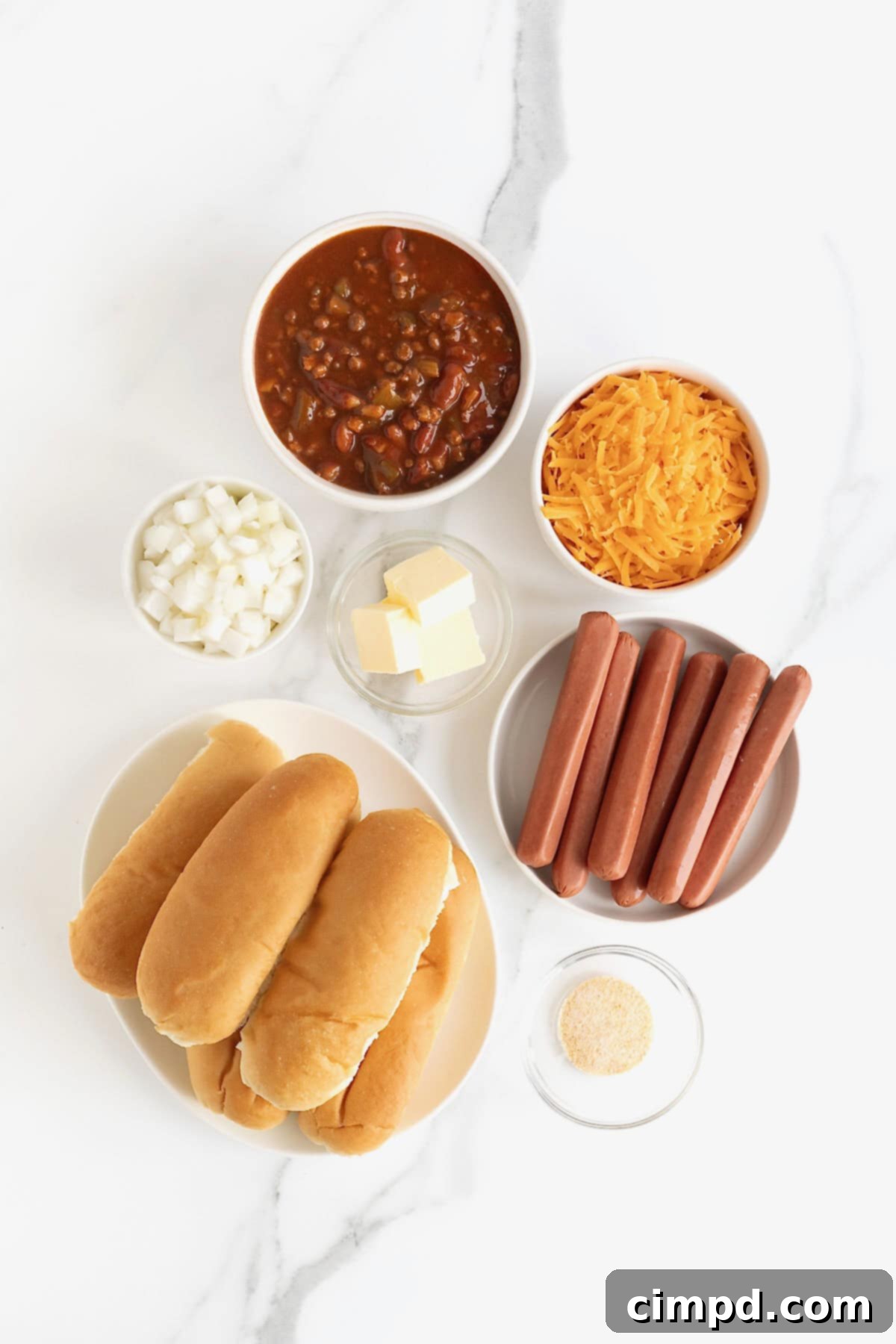 Ingredients to make Chili Cheese Dog Casserole in white dishes on a white marble counter, neatly arranged.