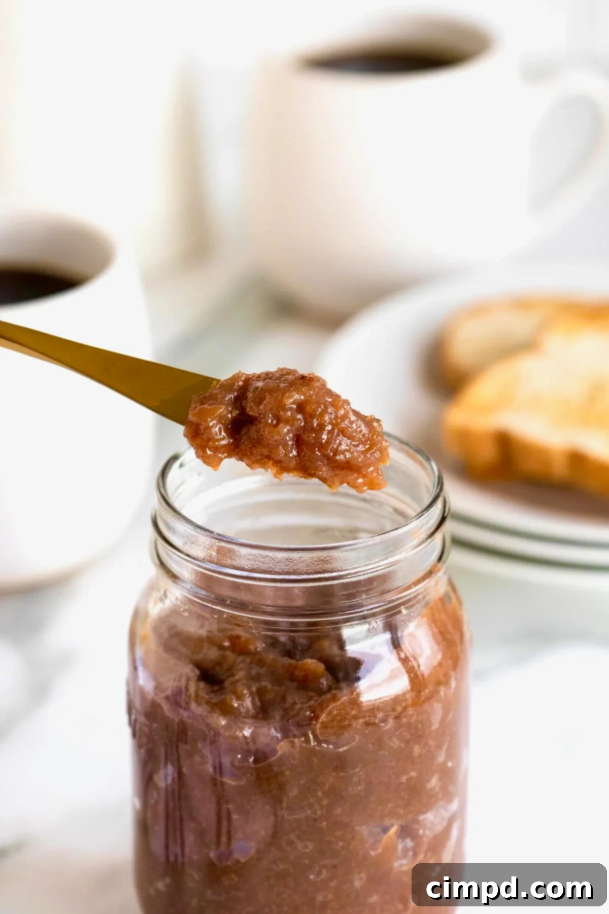Effortless Homemade Grape Jam 3 A glistening spoonful of homemade grape jam held above a rustic glass jar filled with the same delicious preserve.