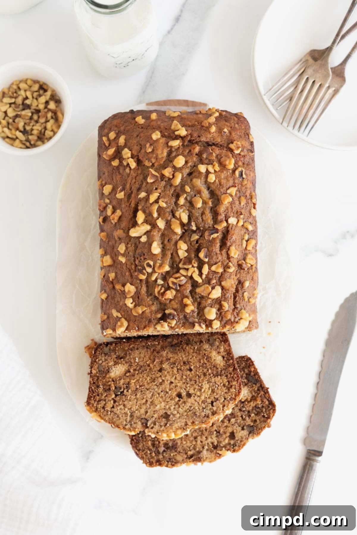 A quarter of a loaf of brown butter banana nut bread, perfectly sliced into two thick pieces, sits on a white cutting board, showcasing its rich texture and walnuts.