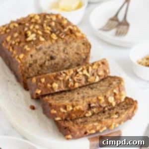 A loaf of banana nut bread on a white cutting board. Half of the loaf is cut into three thick slices.