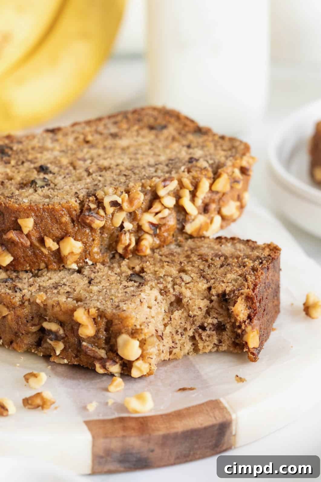 Two perfectly baked slices of brown butter banana nut bread resting on a white marble countertop. One slice has a corner missing, showing the fluffy texture and visible walnut pieces.