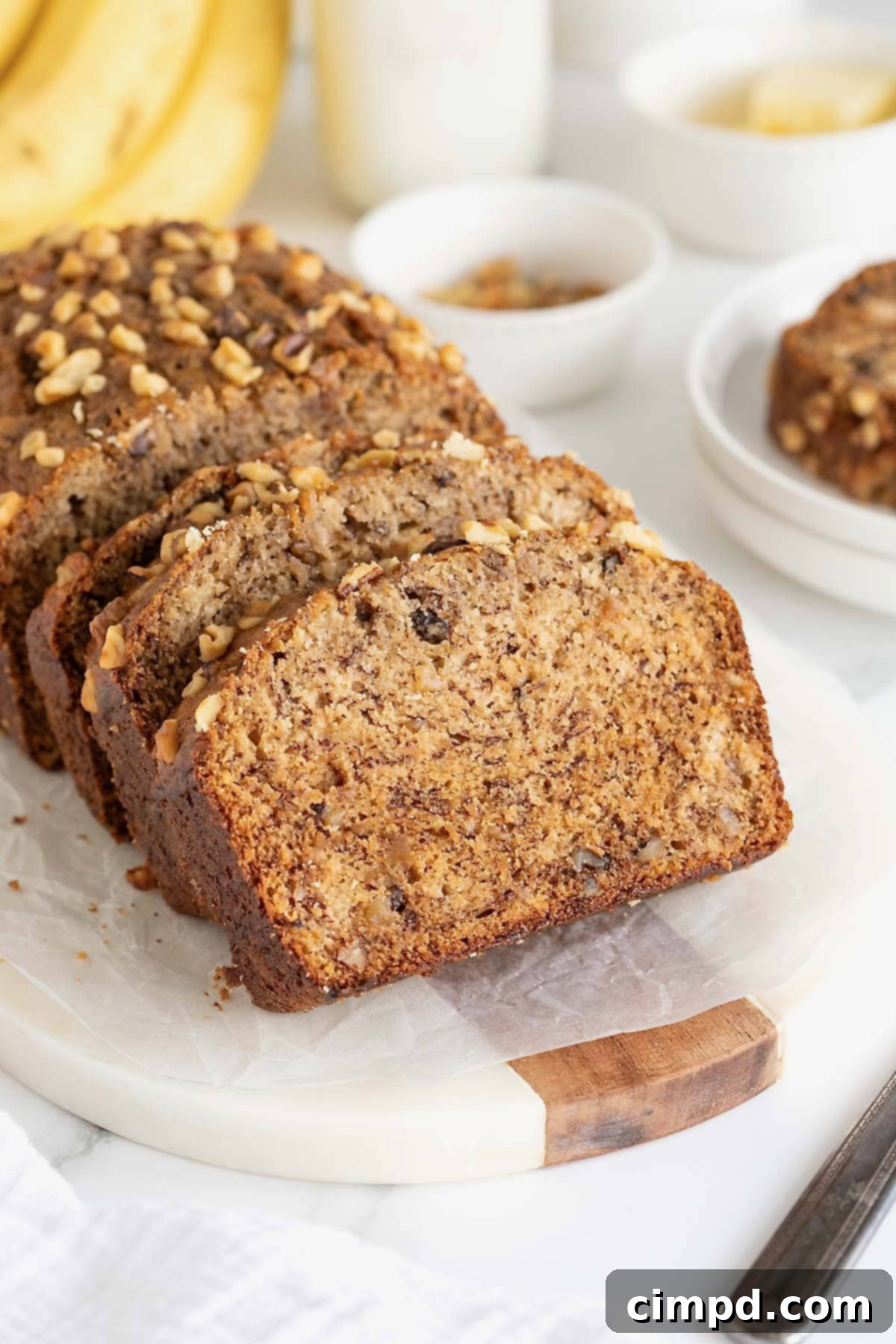 A freshly baked loaf of brown butter banana nut bread on a white cutting board, with several thick slices already cut and ready to enjoy.