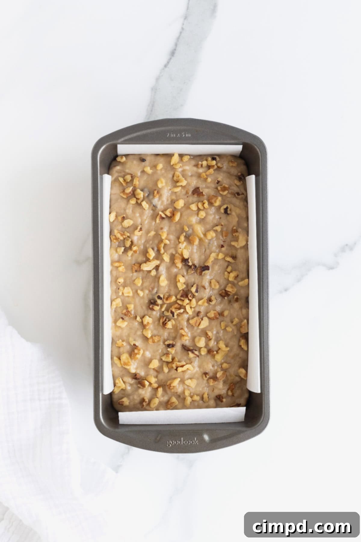 A close-up shot of banana nut bread batter, rich with walnuts, poured into a dark aluminum loaf pan, ready for baking.
