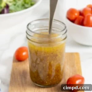 Sparkling Vinaigrette 11 A mason jar of salad dressing with a spoon sticking out of it on a wooden cutting board.