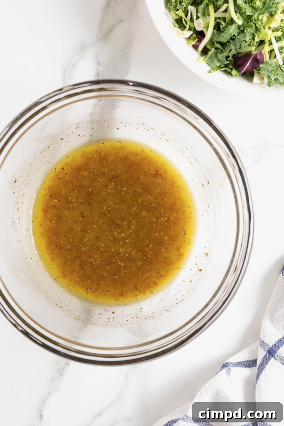 Sparkling Vinaigrette 7 A glass mixing bowl of salad dressing on white marble counter.