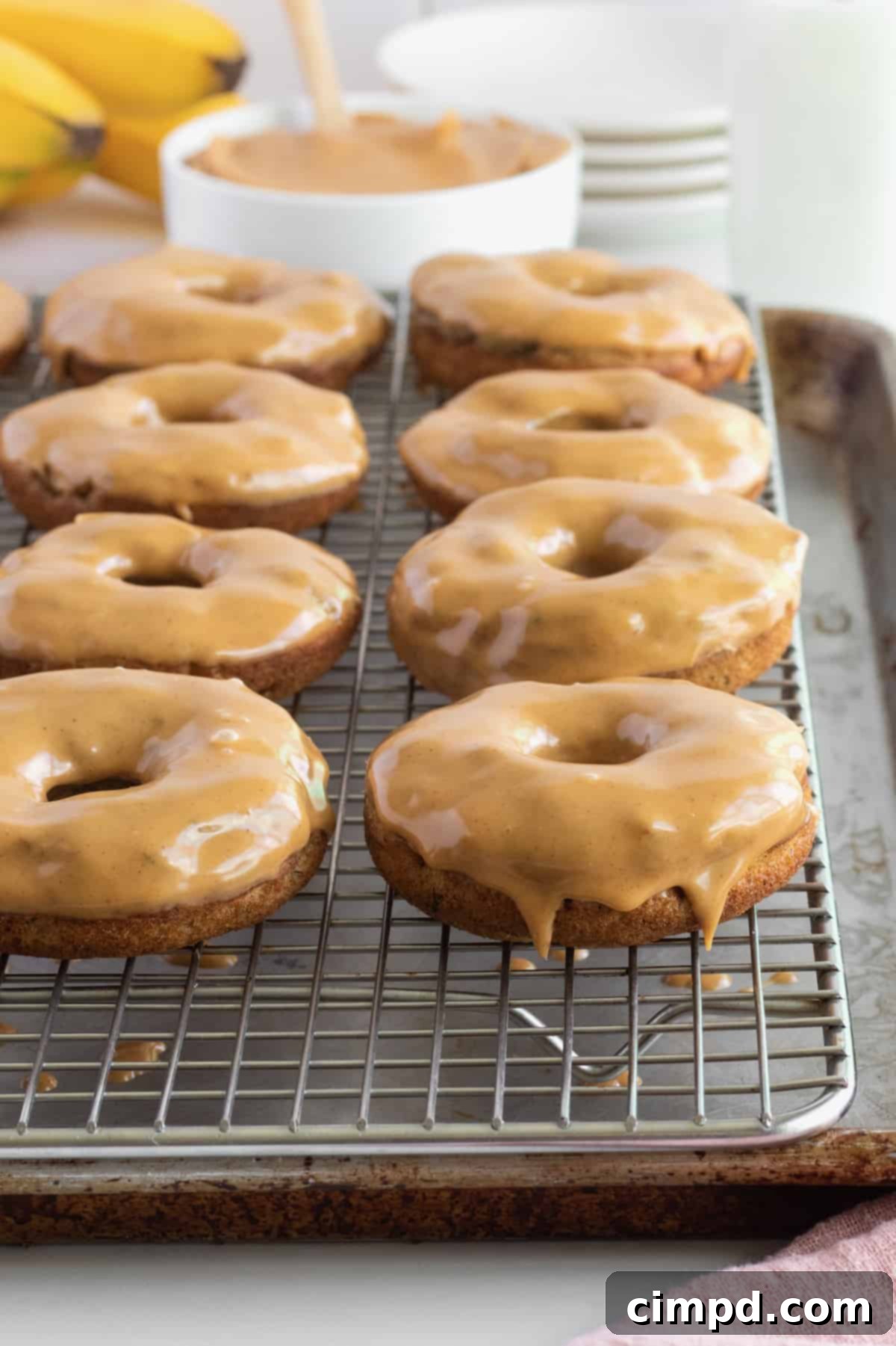 A trio of freshly baked Whole Wheat Banana Donuts with Peanut Butter Glaze, adorned with colorful sprinkles on a wire rack