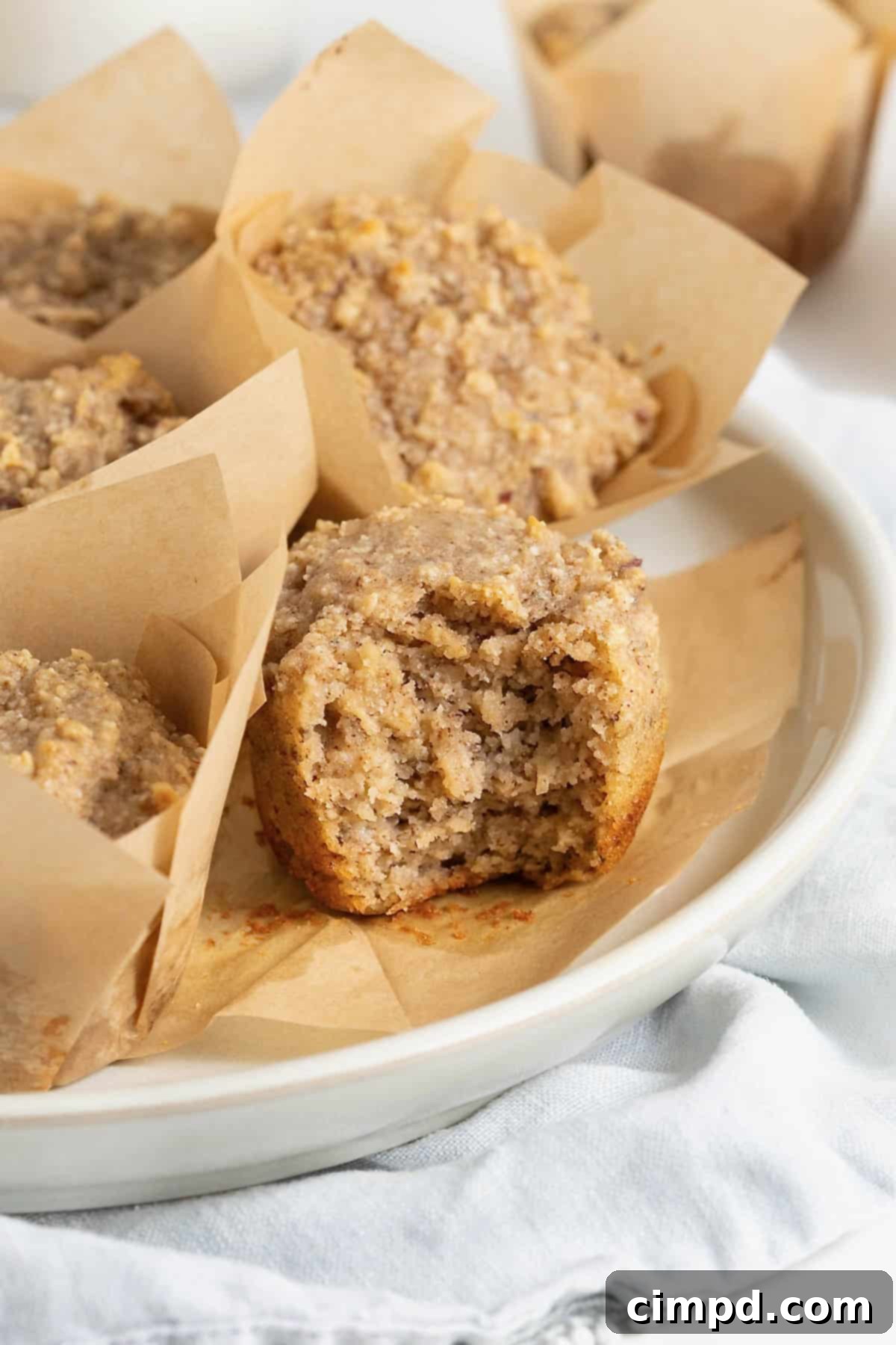 A white plate of tan muffins in brown paper muffin wrappers, ready to be enjoyed.