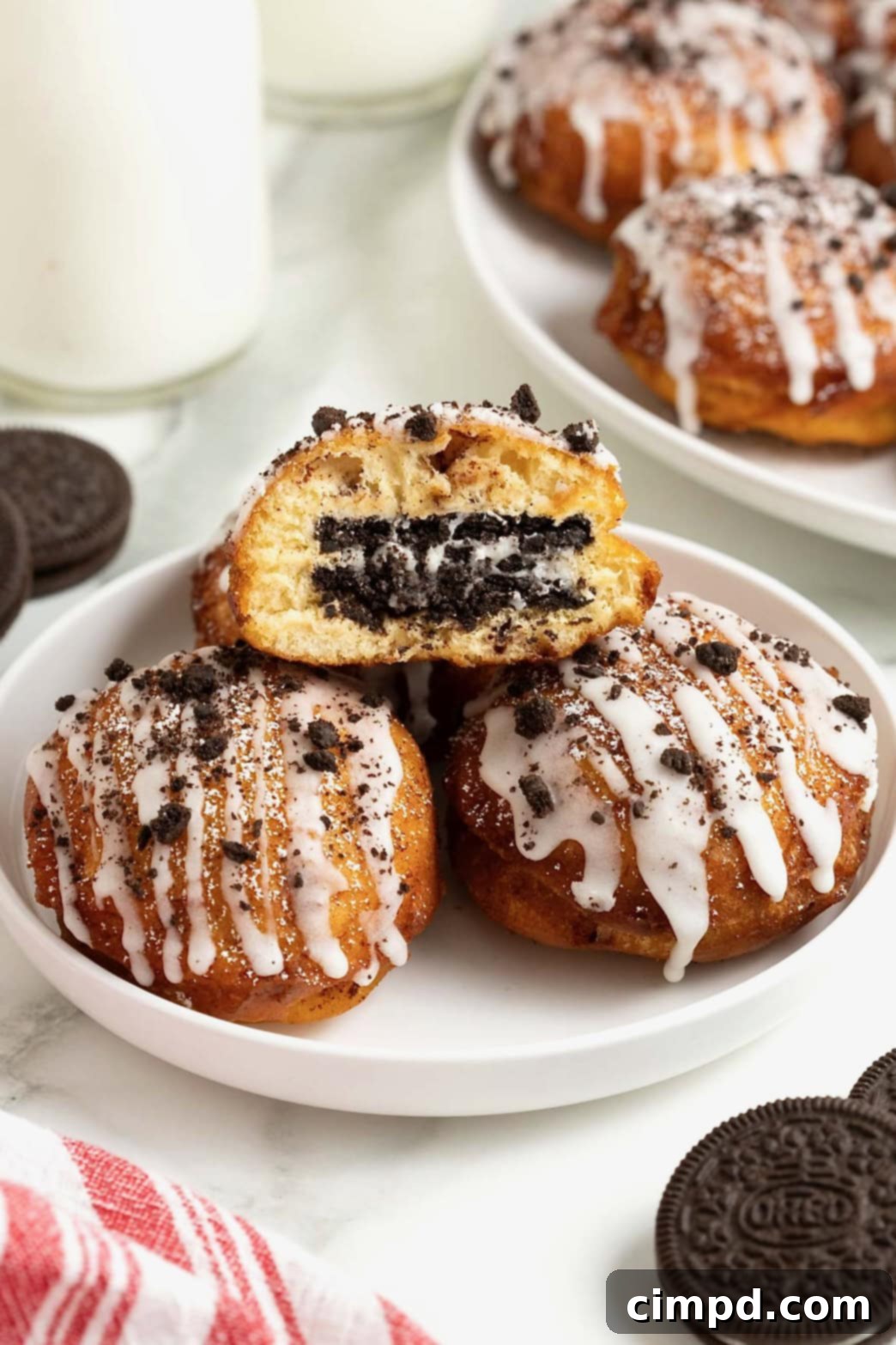 Cinnamon Bun Oreo Fritters 2 A white rimmed plate holding three fried cinnamon rolls with Oreos in the middle. The one of top is cut open to reveal the oreo inside.