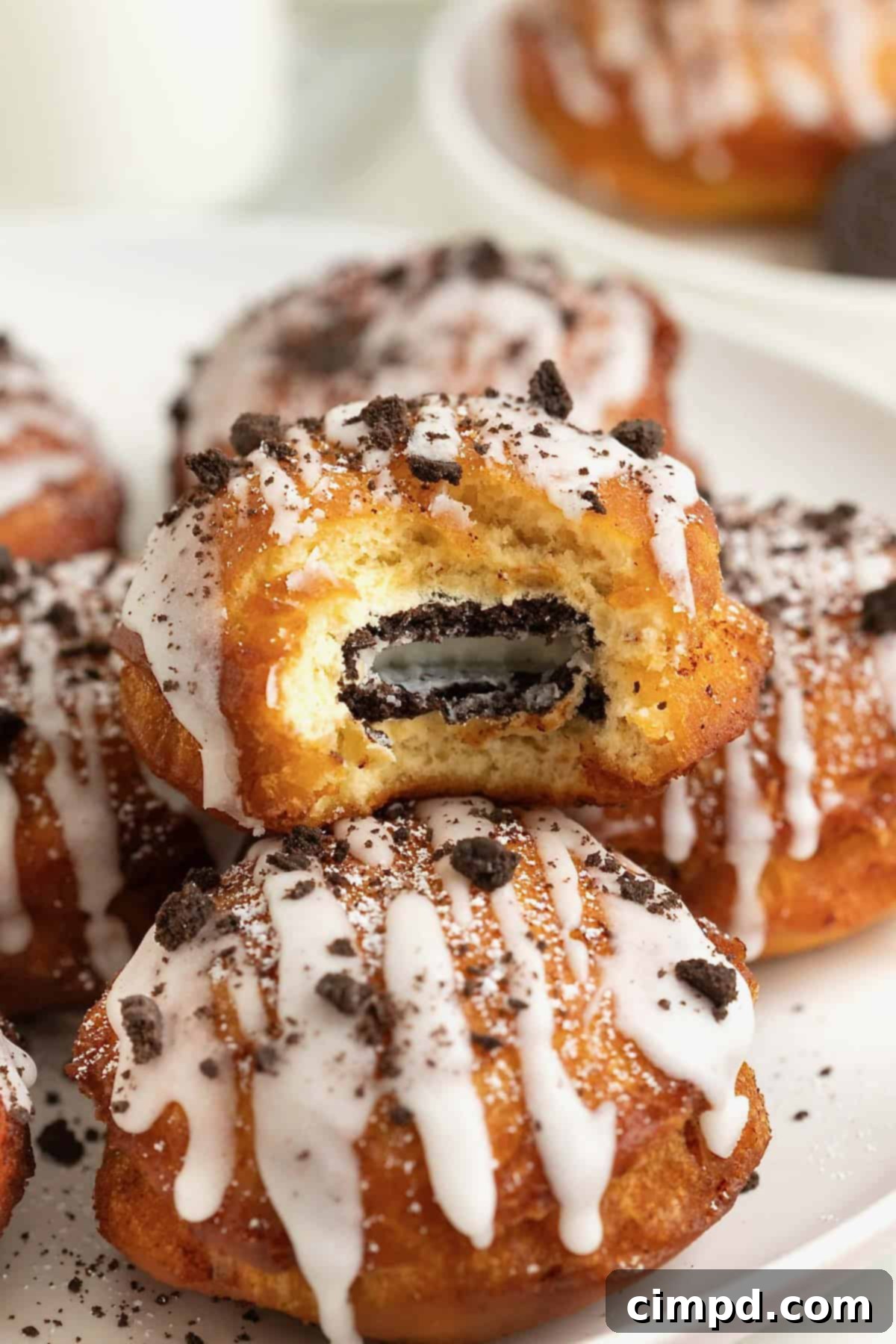 Cinnamon Bun Oreo Fritters 11 A white rimmed plate holding three fried cinnamon rolls with Oreos in the middle. The one of top is cut open to reveal the Oreo cookie inside.