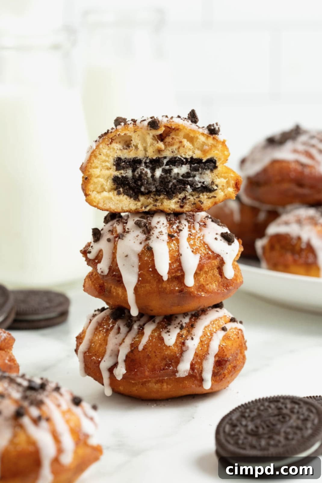 Cinnamon Bun Oreo Fritters 4 A stack of three cinnamon roll fried Oreos on a white marble counter. The top fried Oreo has a bite out of it revealing the Oreo inside.