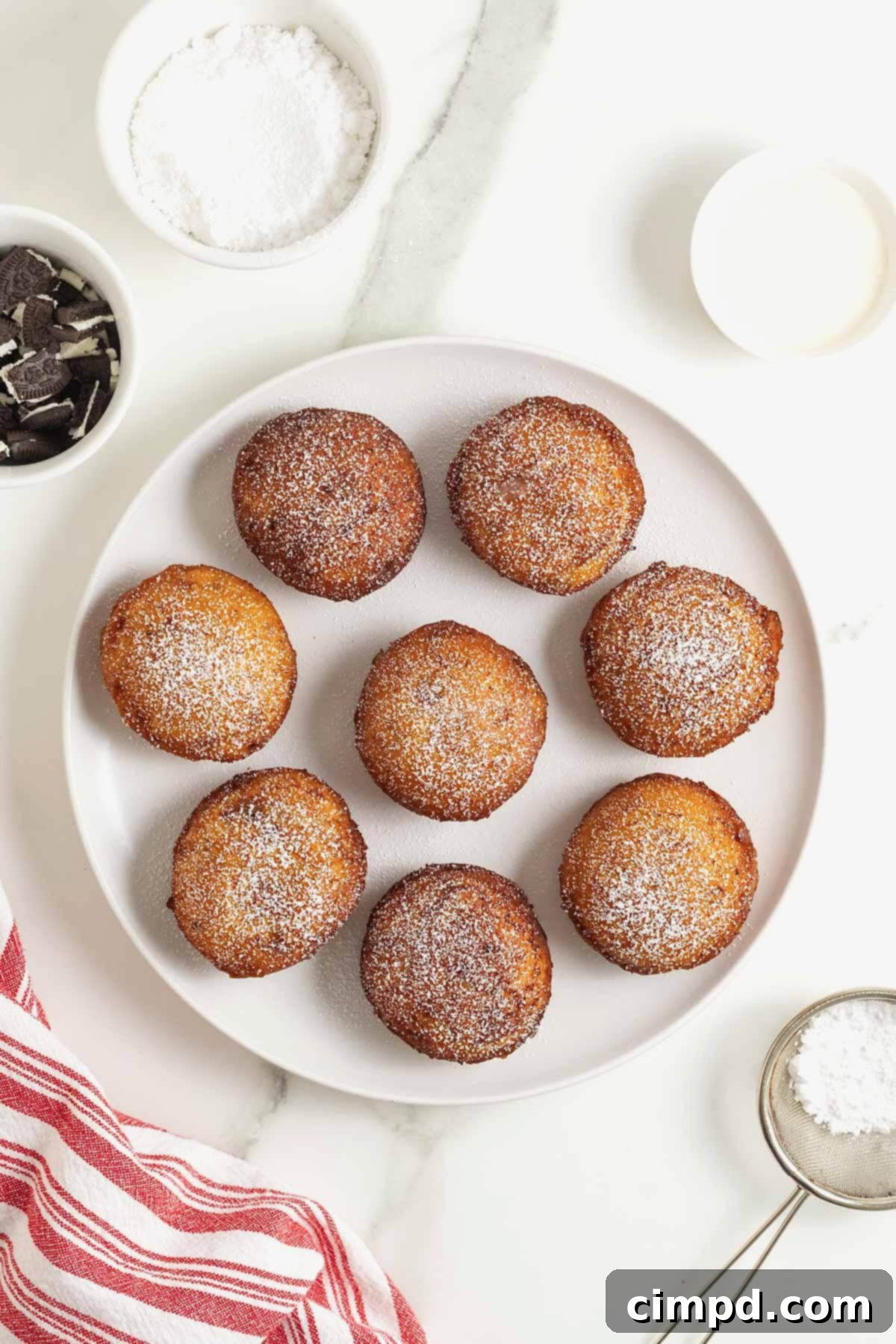 Cinnamon Bun Oreo Fritters 9 A white rimmed plate filled with 8 cinnamon roll fried Oreos dusted with powdered sugar.