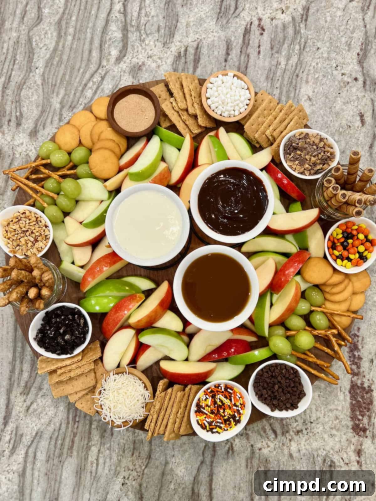 A large round food board filled with slices of red and green apples and an assortment of dipping sauces and garnishes.