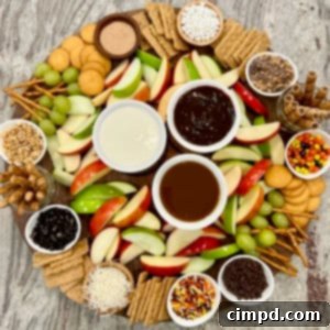 A large round food board filled with slices of red and green apples and an assortment of dipping sauces and garnishes.
