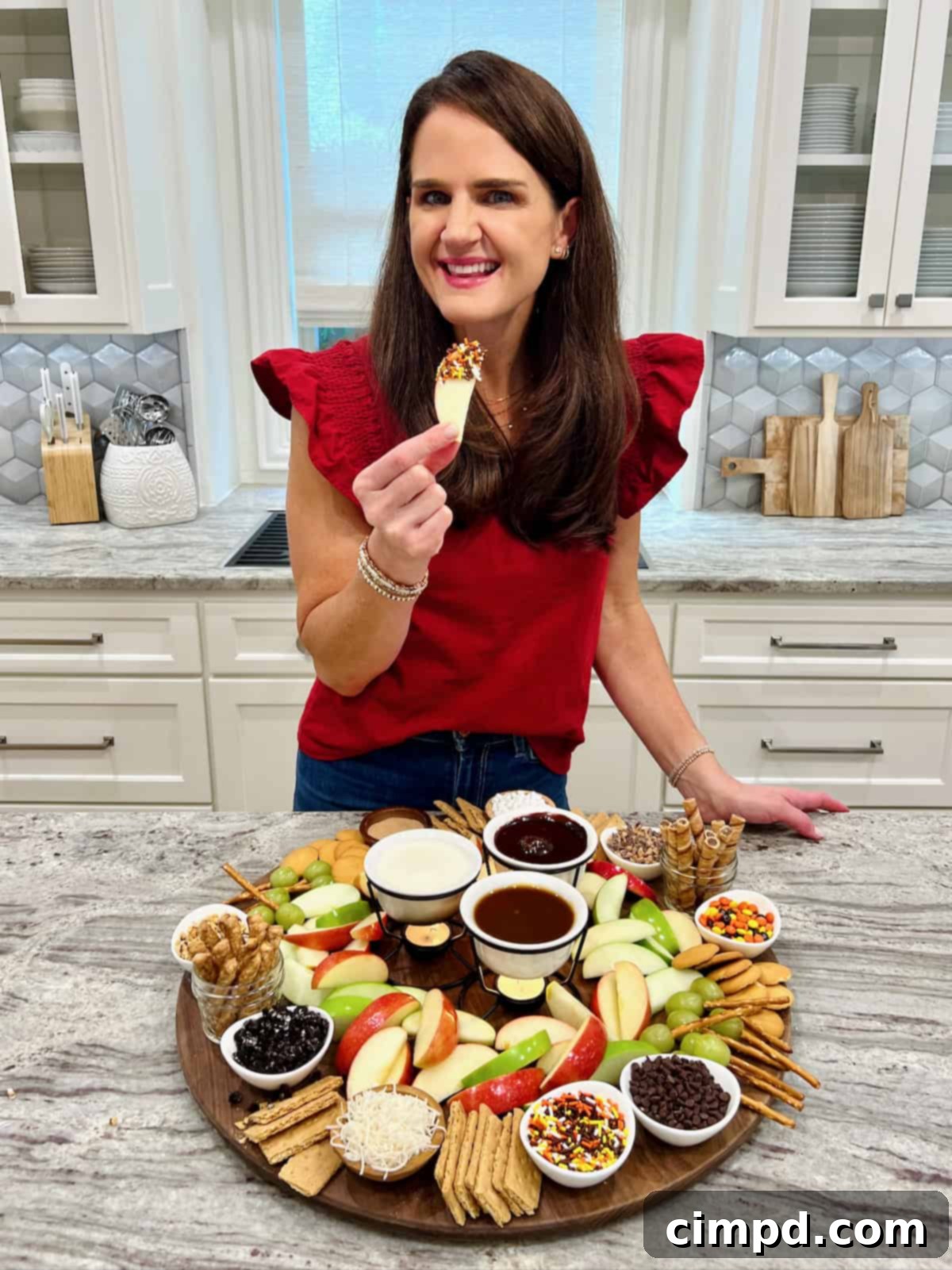 Maegan Brown standing at a gray and white marble counter showing an apple dipping board.