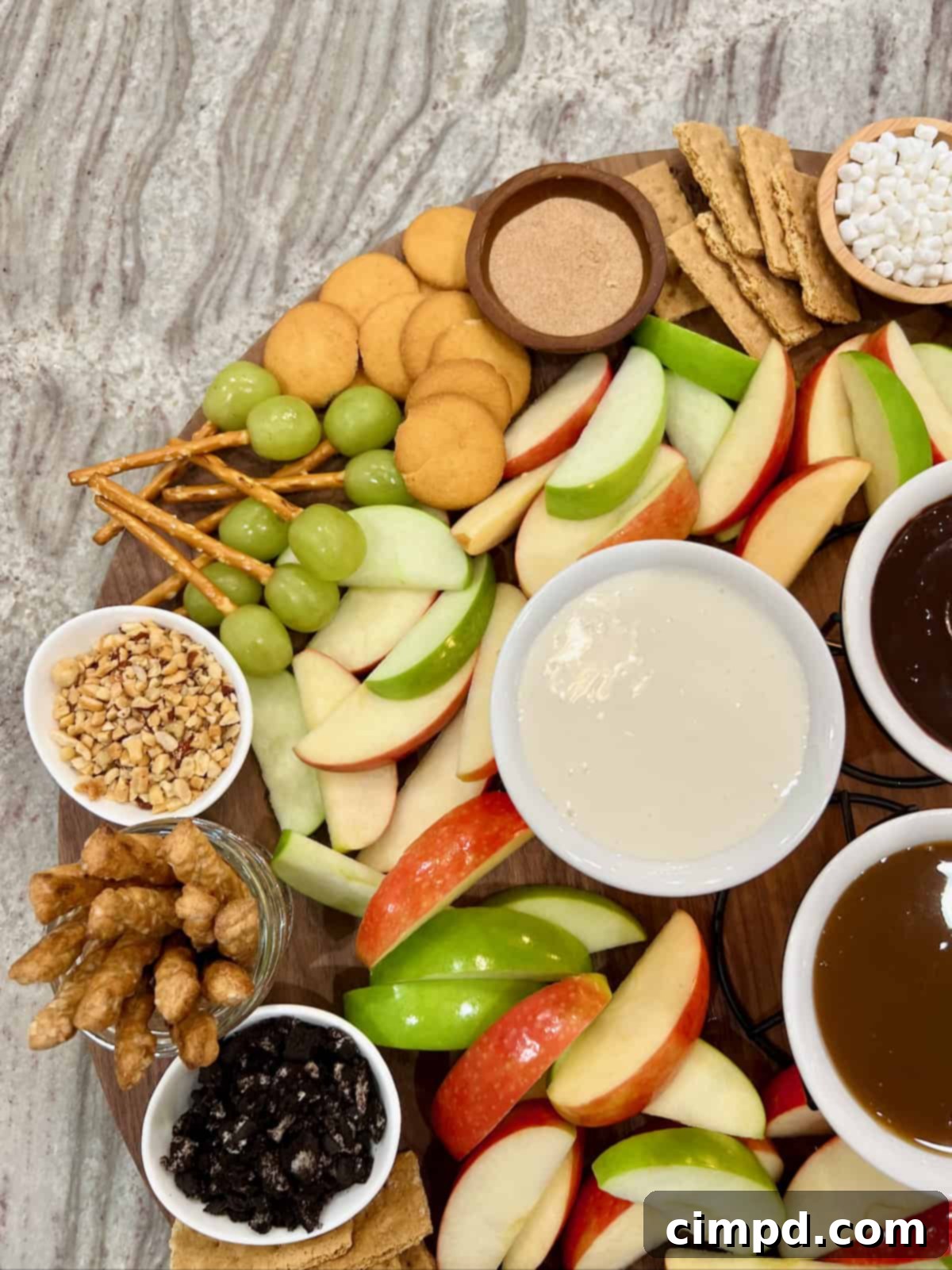 Grapes with pretzels stuck into them next to Nilla wafers and a small white bowl of crushed nuts on a large round wood food board.