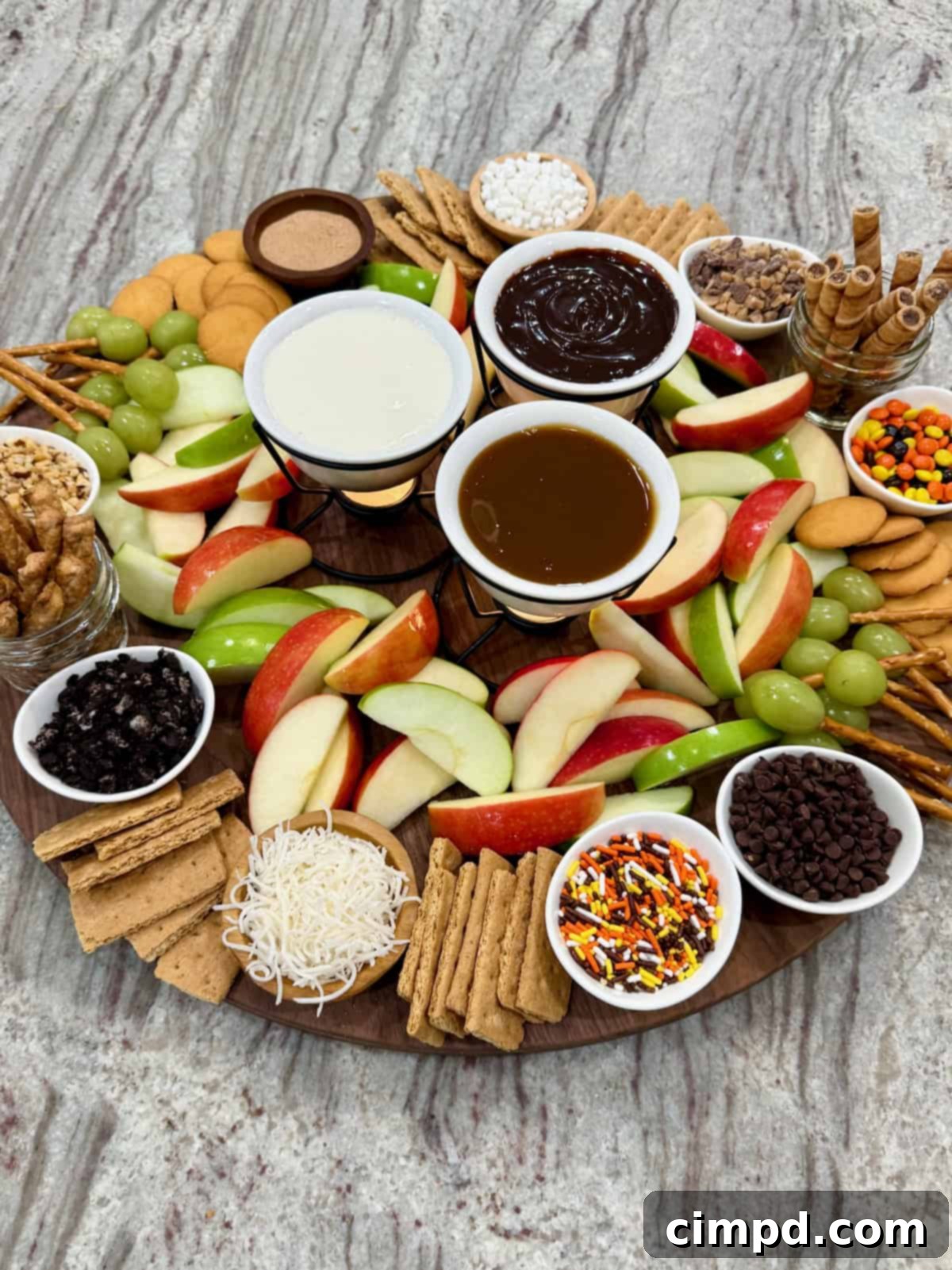 A large round food board filled with slices of red and green apples and an assortment of dipping sauces and garnishes.
