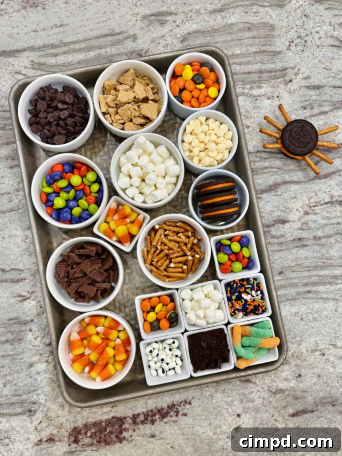 Various ingredients for Halloween Cookie Bars arranged in small glass dishes within a rimmed baking sheet, ready for mixing.