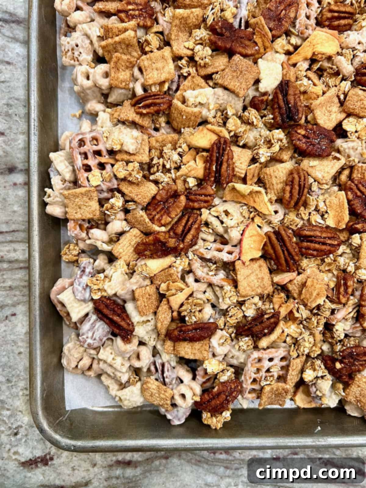 A generous serving of Apple Pie Snack Mix beautifully displayed on a parchment-lined baking sheet, ready for either enjoyment or elegant packaging as a gift.