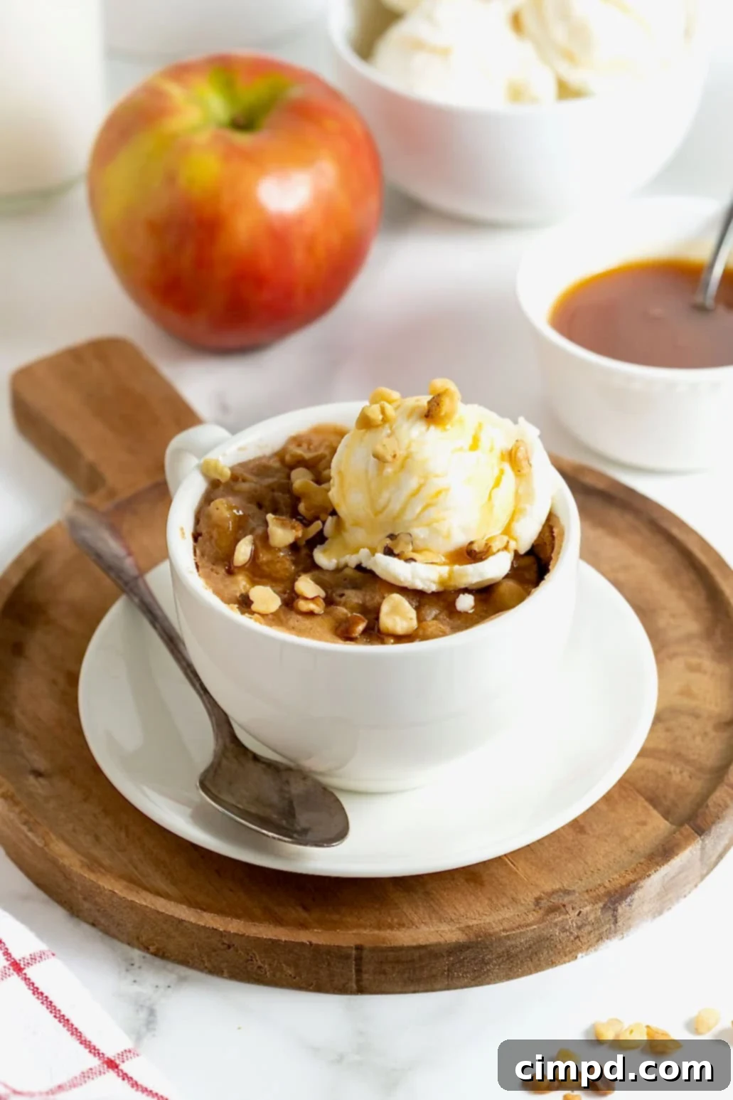 Spiced Apple Mug Delight 2 A perfectly baked apple mug cake, topped with a scoop of vanilla ice cream, resting on a rustic wooden cutting board. The cake's golden-brown crust hints at the warm, spiced apples within.