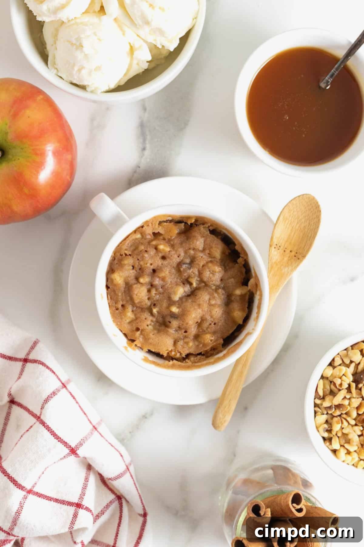 Spiced Apple Mug Delight 11 A perfectly garnished apple mug cake with ice cream and caramel, surrounded by small dishes of vanilla ice cream, chopped walnuts, and warm caramel sauce, inviting immediate enjoyment.