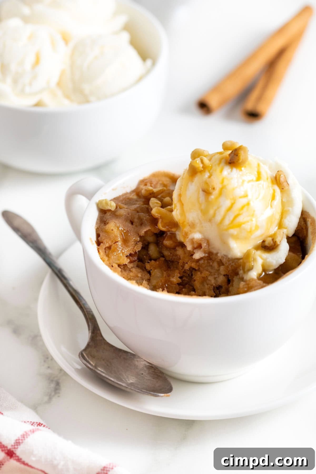 Spiced Apple Mug Delight 3 A close-up of an apple mug cake with a spoon, showing a bite taken out of the fluffy, spiced cake. A scoop of ice cream melts slightly on top, enhancing its appeal.