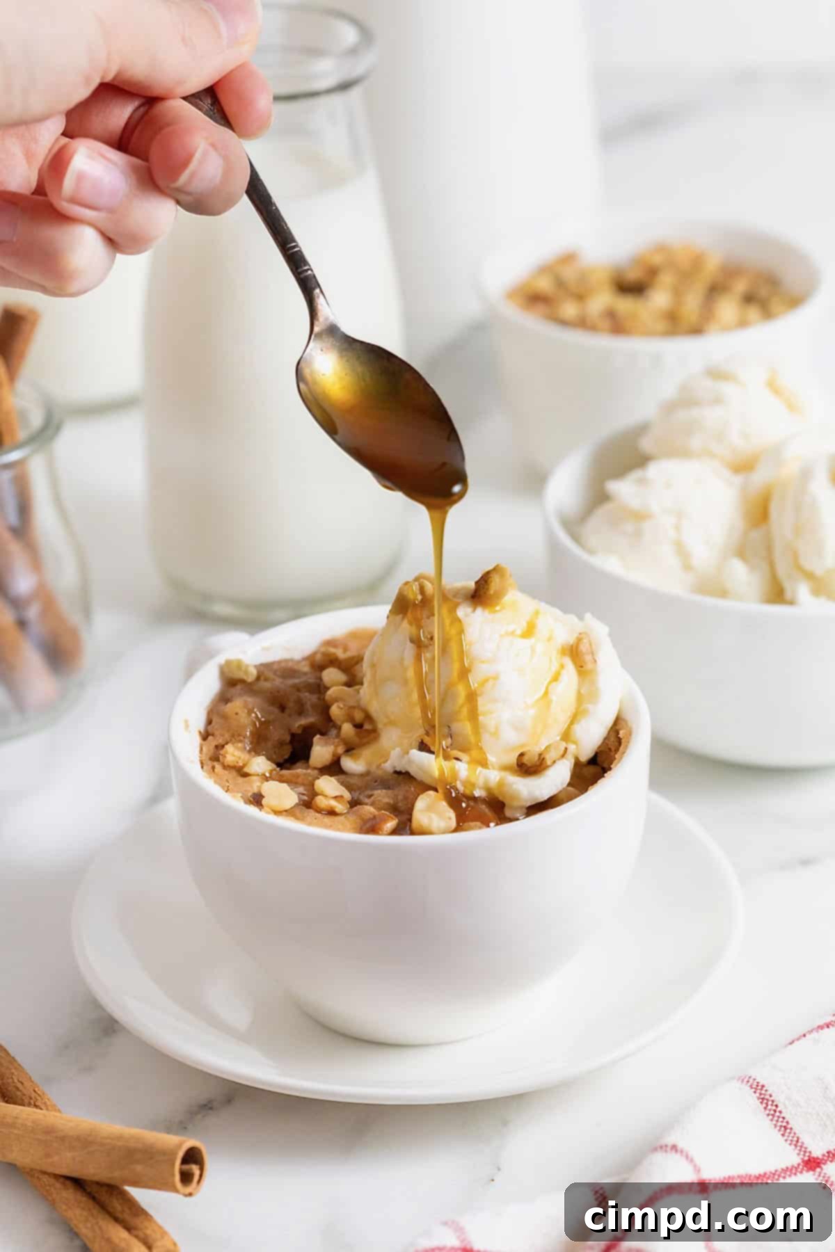 Spiced Apple Mug Delight 4 Caramel sauce being drizzled over a scoop of vanilla ice cream atop a warm apple mug cake, presented on a white plate. The steam subtly rising suggests its freshly baked goodness.