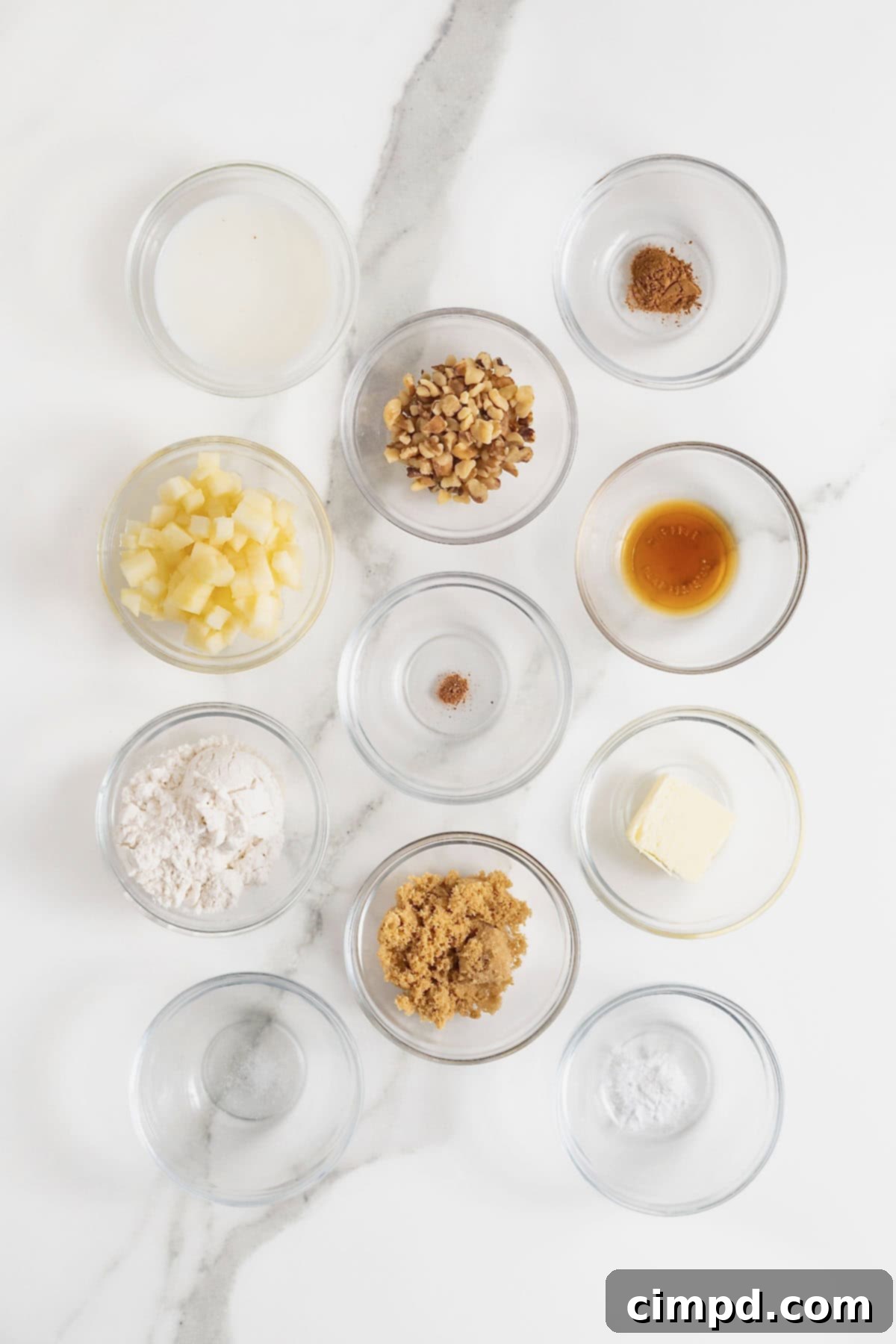 Spiced Apple Mug Delight 6 A collection of measured ingredients for making a microwave apple cake, neatly arranged in small glass bowls on a white marble countertop. This showcases the preparation stage with care and precision.