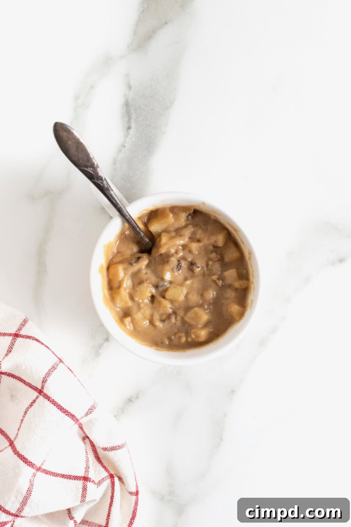 Spiced Apple Mug Delight 8 A close-up shot of apple cake batter, perfectly mixed with apple chunks and walnuts, ready for microwaving in a white mug on a pristine white marble counter.