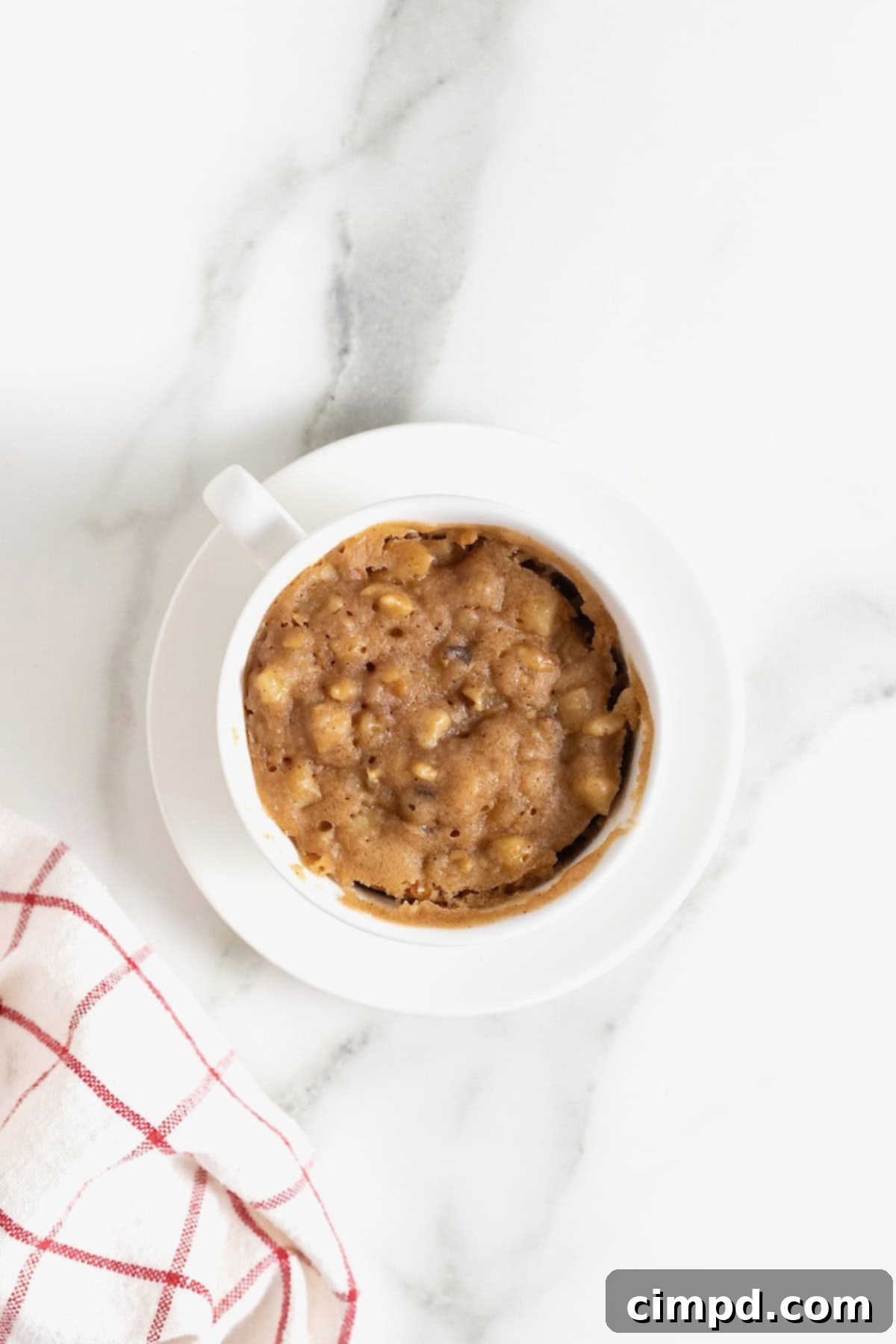 Spiced Apple Mug Delight 10 A freshly microwaved apple mug cake, golden and risen, still warm in its white mug on a white marble countertop, exuding a comforting aroma.