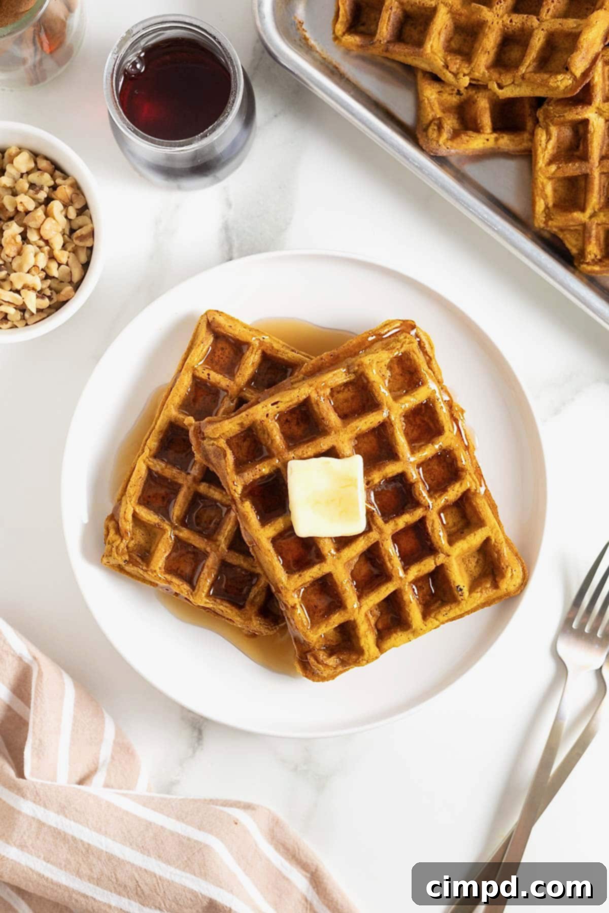 Spiced Pumpkin Waffles 2 Two golden-brown pumpkin waffles gently overlapping on a pristine white plate, crowned with a square of melting butter.