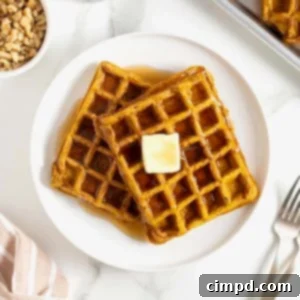 Spiced Pumpkin Waffles 12 Two pumpkin waffles laying overlapping on a white plate. There is a square of butter on the top waffle.