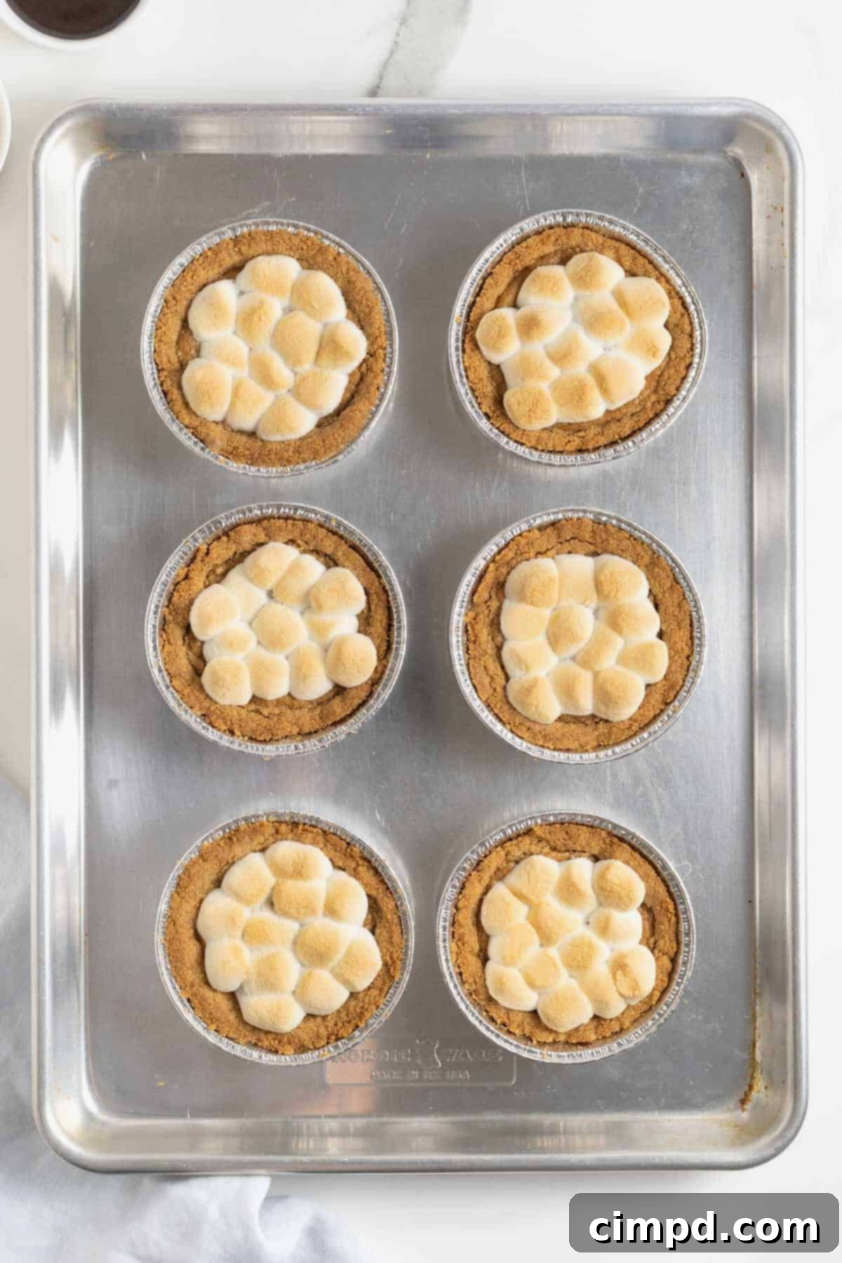 Close-up of mini s'mores cookie pies after the second bake, showing perfectly puffed and golden-brown melted marshmallows, creating a soft, gooey topping.