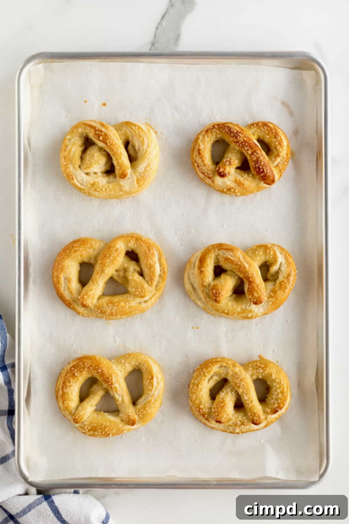 Six freshly baked, golden-brown homemade soft pretzels cooling on a parchment-lined baking sheet, ready to be enjoyed.