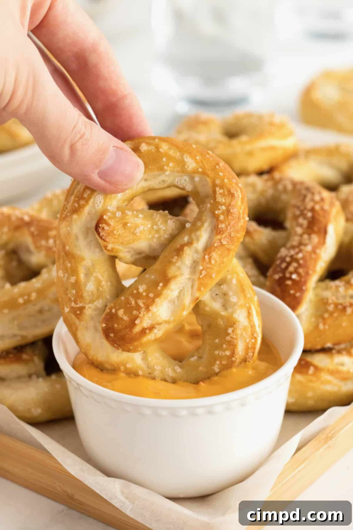 A hand dipping a homemade soft pretzel into a small dish of warm, golden, and creamy cheese sauce, a perfect pairing.