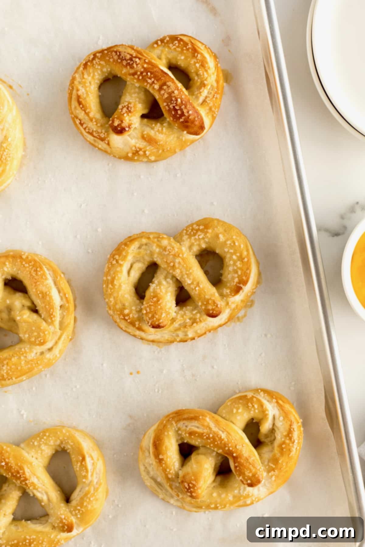 Six perfectly arranged soft pretzels on a parchment-covered aluminum rimmed baking sheet, ready for storage or reheating.