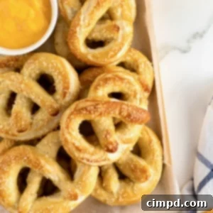 A wooden tray filled with soft pretzels and a small white dish of cheese sauce.
