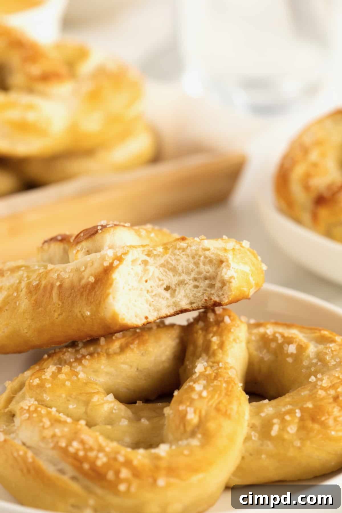 A delectable pile of homemade soft pretzels on a white serving plate, with a bite playfully taken out of the top pretzel, highlighting its soft interior.